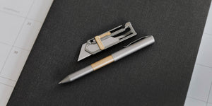 EDC gear pocket knife and titanium pen sitting on notebook