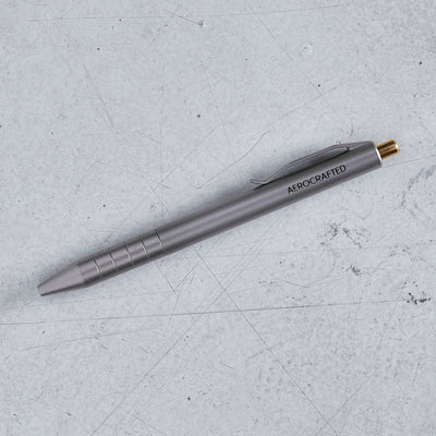 the retract titanium click pen on the ground of our california hanger showing off it's bronze clicker and titanium tumbled sheen #material_titanium-bronze