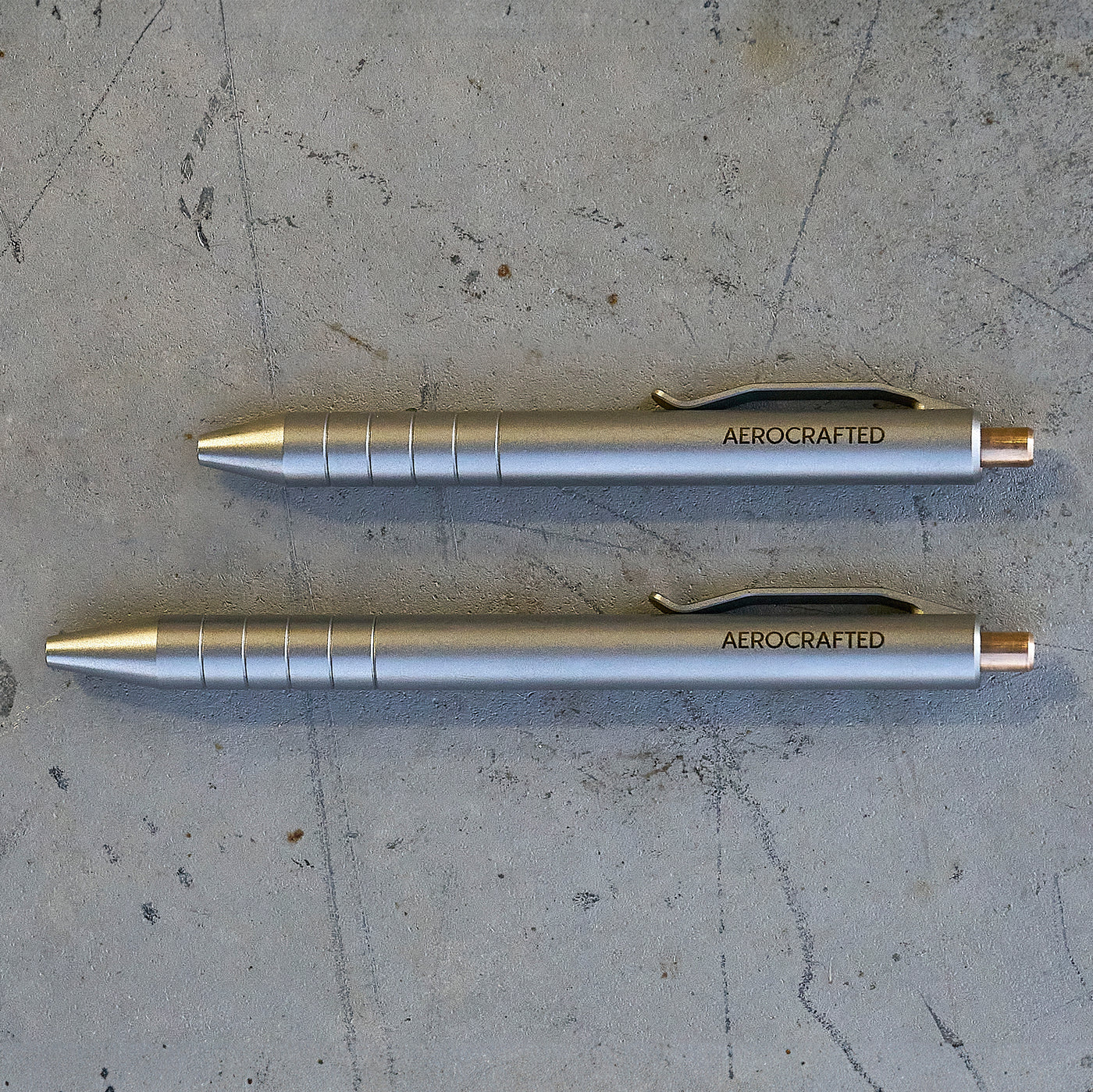 two titanium pens showing the size difference between the smaller and larger retract click pen both cnc machined by aerospace engineers and pilots in california #material_titanium-bronze
