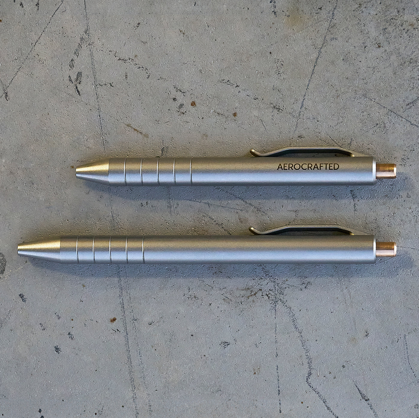 two titanium pens showing the size difference between the smaller and larger retract click pen both cnc machined by aerospace engineers and pilots in california #material_titanium-bronze