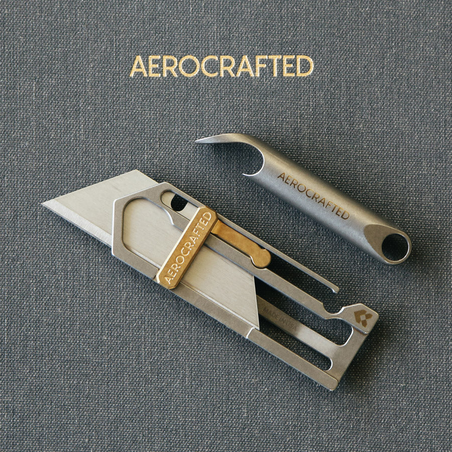 a wingman titanium bottle opener and a sideslip titanium utility knife laying on a notebook all made in the usa and designed by aerospace engineers #material_titanium