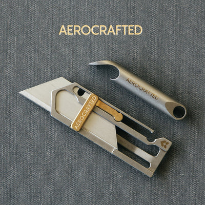 a wingman titanium bottle opener and a sideslip titanium utility knife laying on a notebook all made in the usa and designed by aerospace engineers #material_titanium